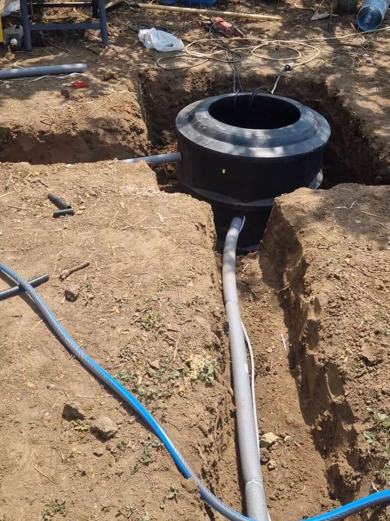 Cămin negru de polietilenă așezat în groapă, cu țeava de racord spre casă pe fundul șanțului și furtunul albastru alături, la o lucrare din Balotești