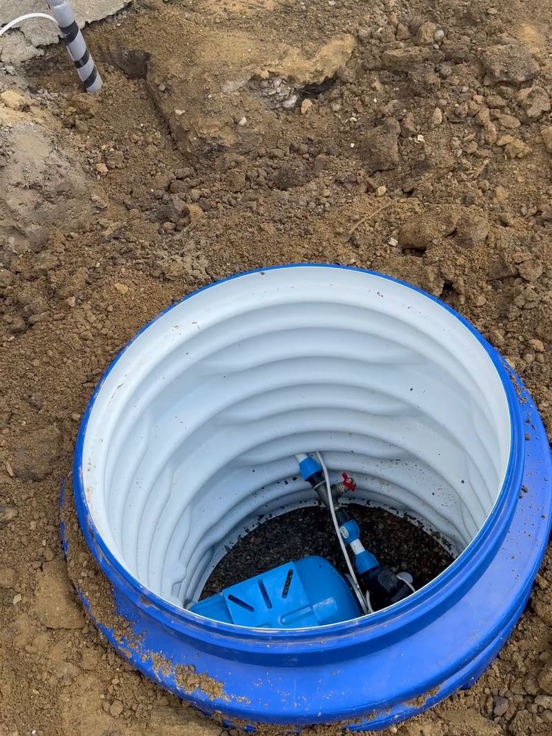 Cămin de vizitare din plastic albastru, alb pe dinăuntru, îngropat în pământ proaspăt săpat; pe fundul lui, hidroforul albastru și racordurile pompei
