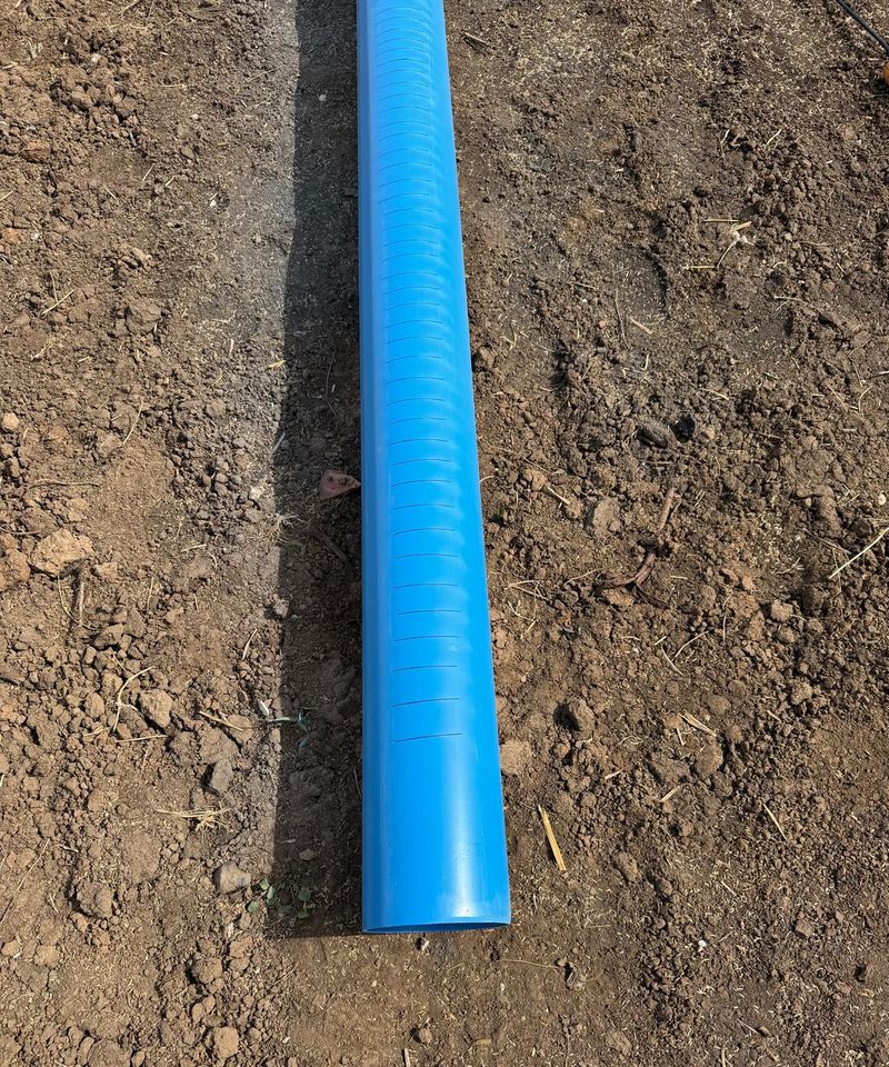 Țeavă albastră de PVC pentru filtrul puțului, cu fante tăiate transversal pe o porțiune, pe pământul săpat