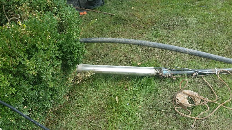 Pompă submersibilă din inox scoasă din puț și așezată pe iarbă, cu furtunul de refulare și frânghia de siguranță