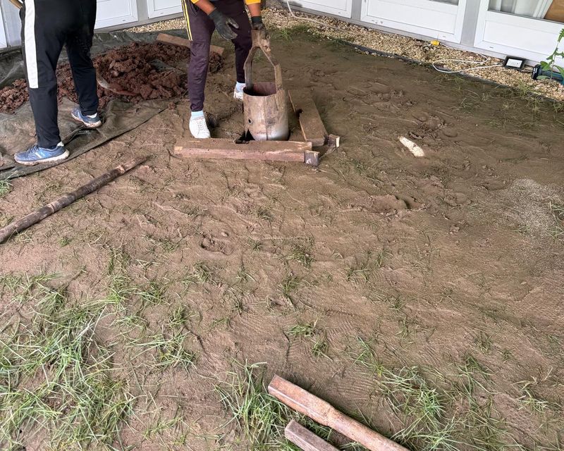 Lingura de foraj ridicată la gura găurii, între scândurile de sprijin, sub cort, cu mâinile în mănuși și pământul scos