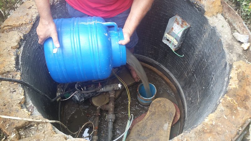 Un om toarnă apă dintr-un bidon albastru în puțul cu inele de beton, lângă pompa submersibilă, august 2016