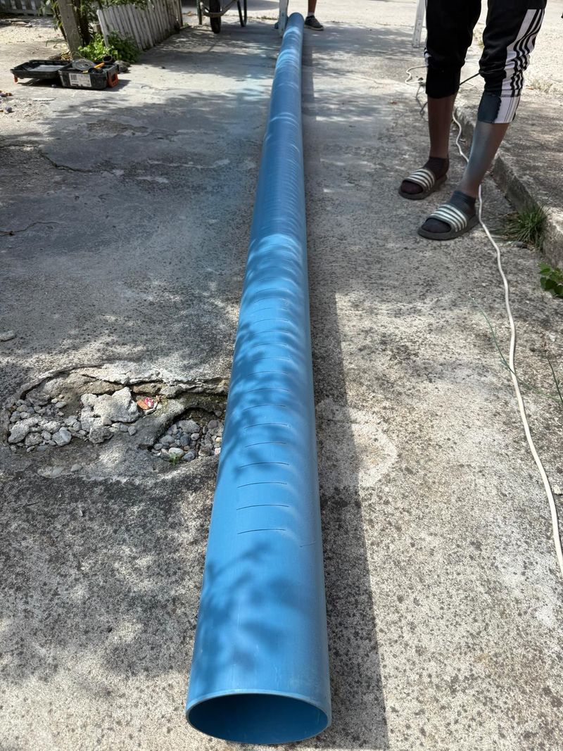 Tub albastru de PVC cu fante, întins pe o alee de beton, pregătit pentru retubarea unui puț din tuburi de beton
